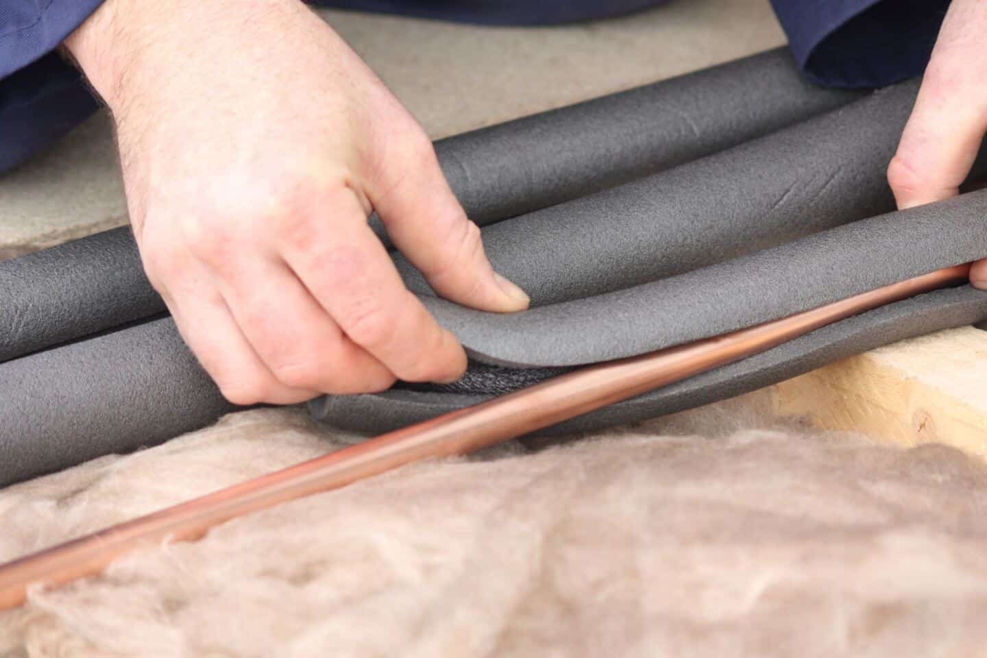 Male hands fit foam lagging around pipework to ensure good plumbing maintenance