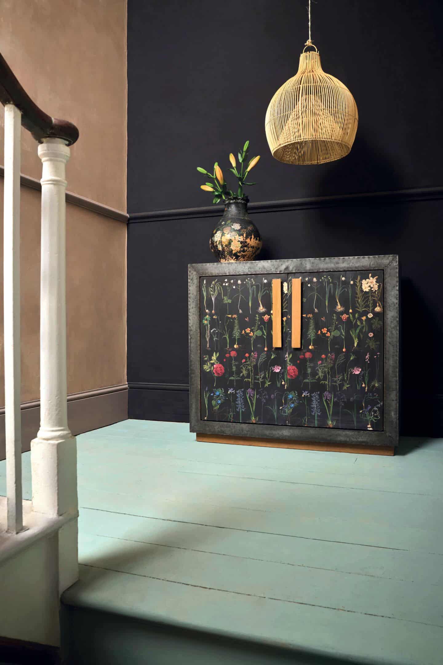 Hallway with black and brown walls and green painted floorboards with a decoupage cabinet against the wall