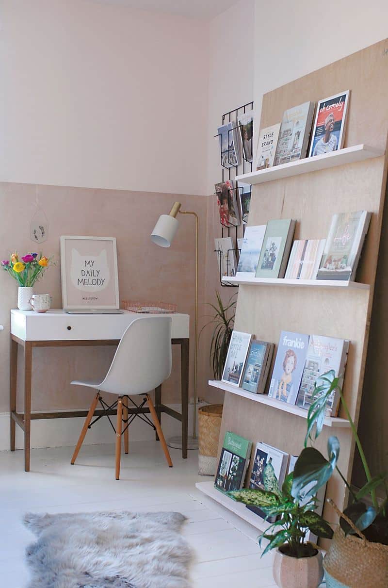 A small office space in the corner of a room uses leaning shelves to avoid damaging the wall