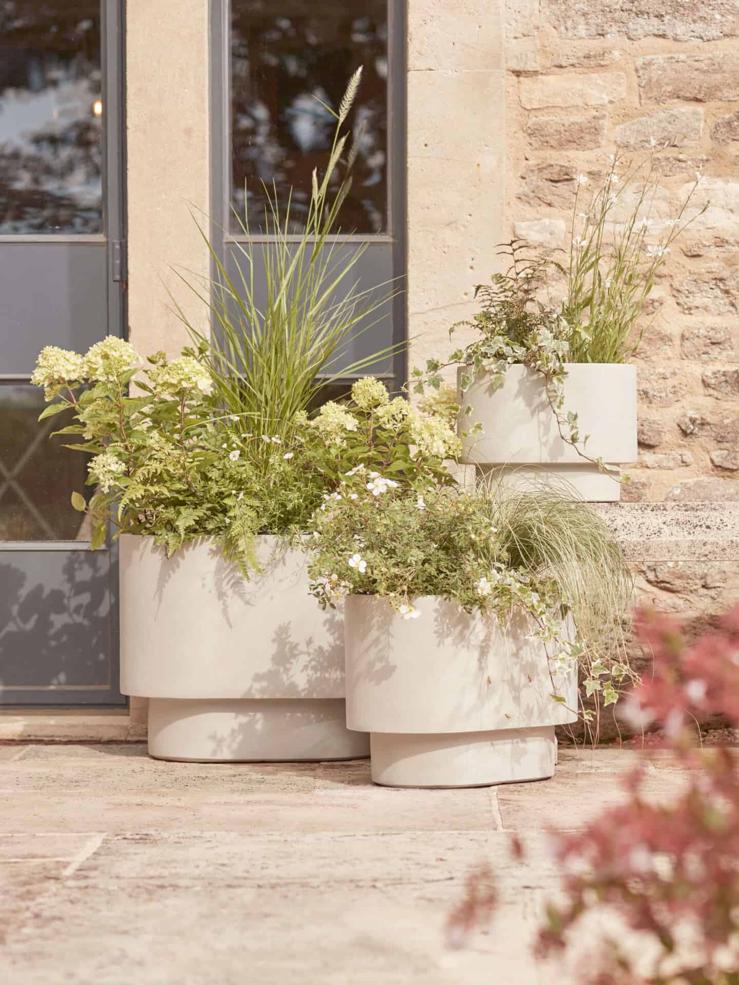 3 Beige planters full of plants on a patio
