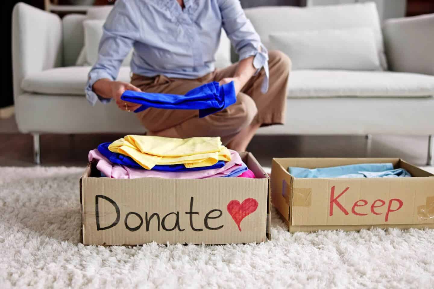 A white woman sat on a sofa decluttering her home by putting clothing into labelled boxes