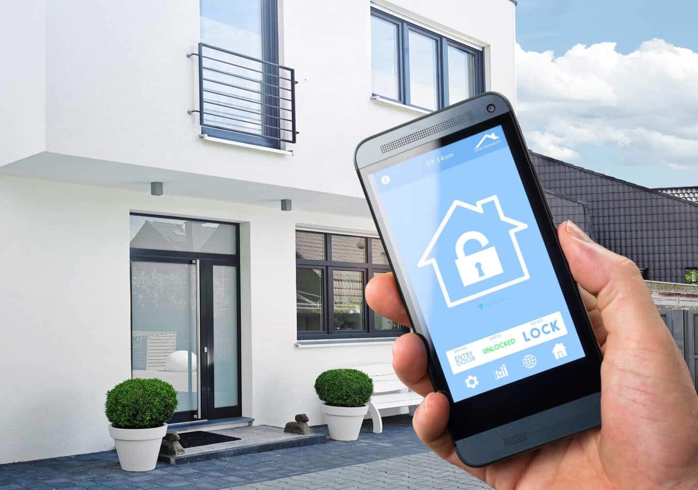 A man holding a smart phone displaying a home security app. A modern home is in the background
