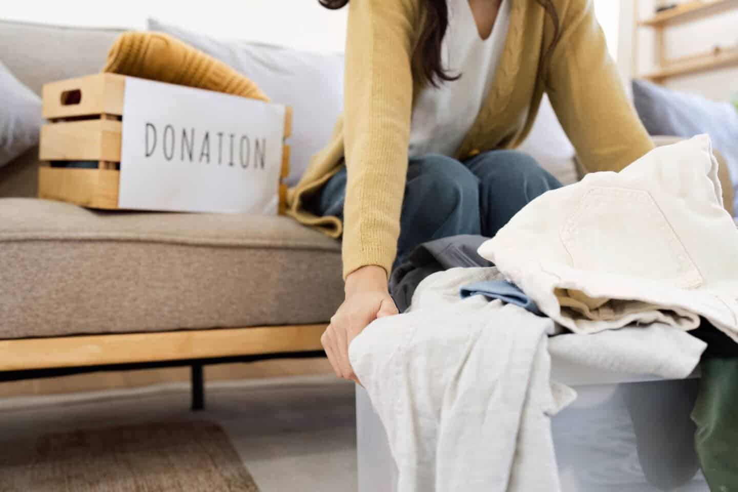 A white woman sat on a sofa decluttering her home by putting clothing into crates and bags