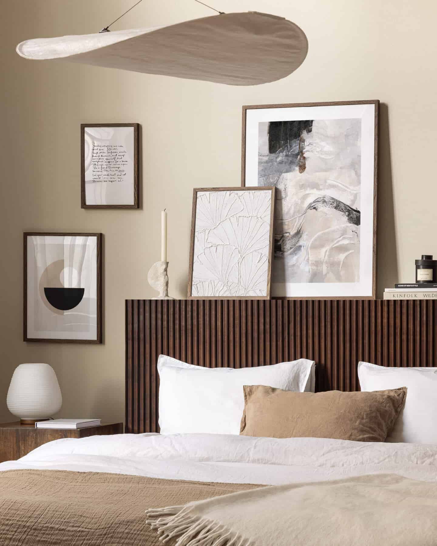 A bedroom in shades of brown. Frames lean against the wall on a ledge behind the bed