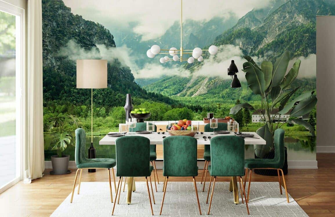 Ever Wallpaper mural of mountains covered in trees behind a modern dining table with green velvet chairs with gold legs.