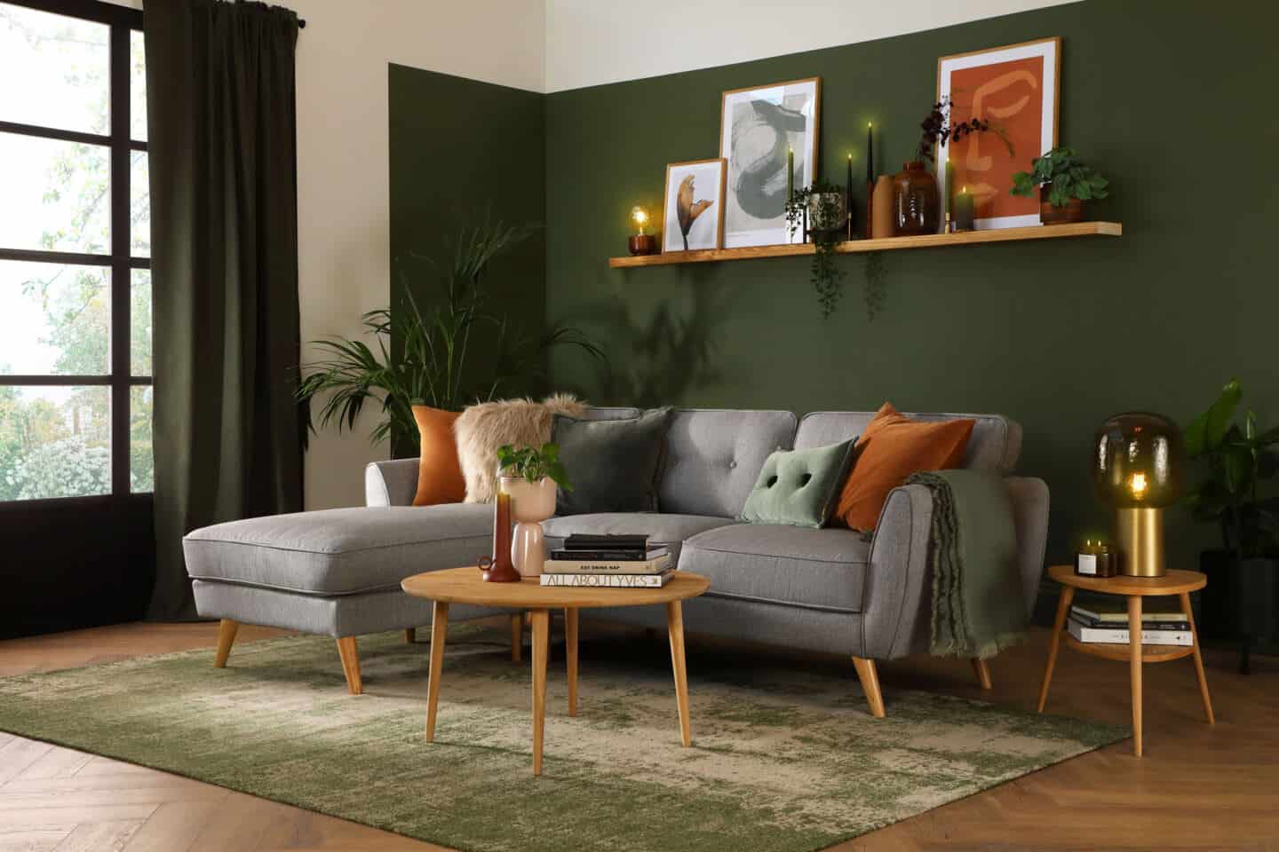 A grey chaise service in a dark green living room with large floor-to-ceiling window. A floating shelf is behind the sofa.