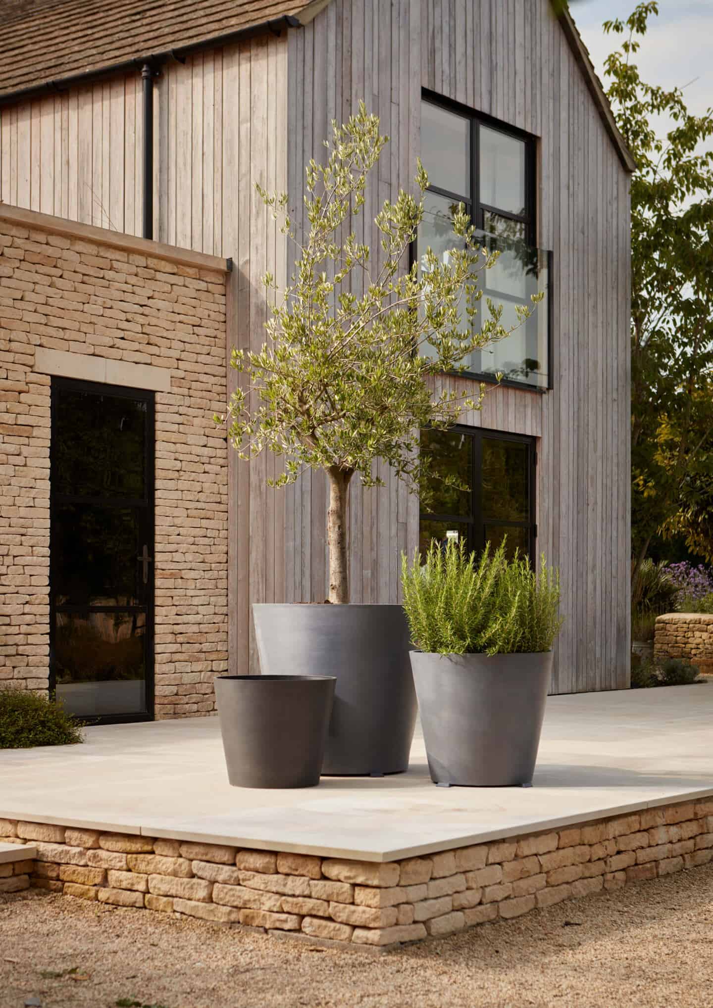 3 large planters stood in the garden of a modern home clad with wood