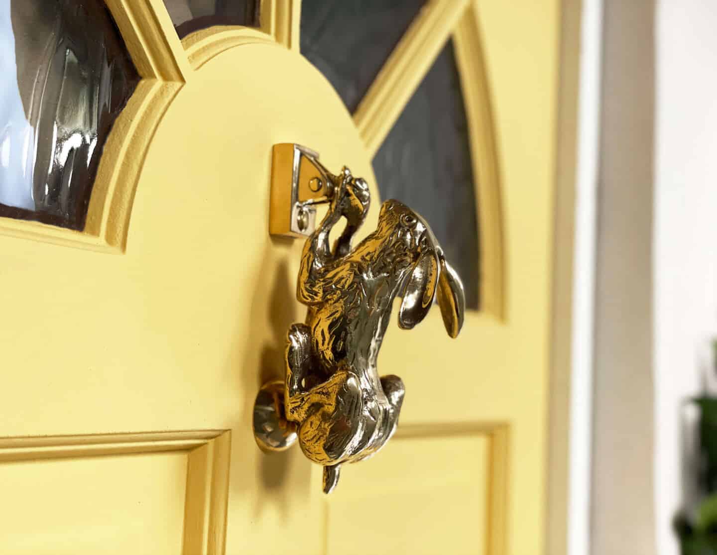 A golden hare door knocker mounted on a yellow wooden front door