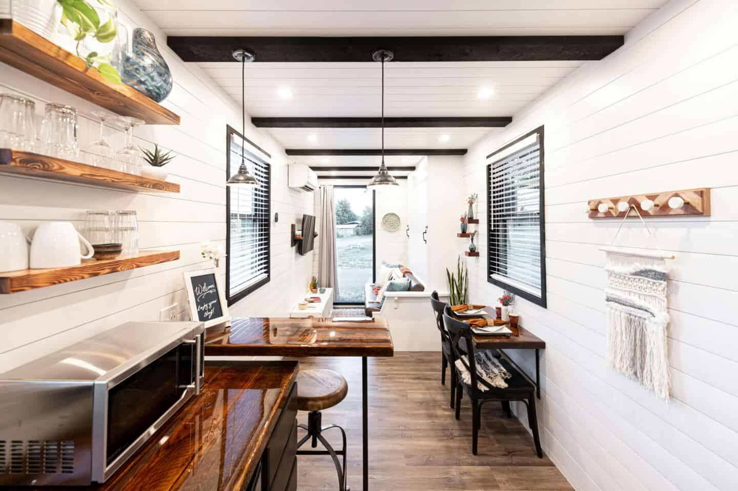 A small home with white shiplap walls, an open plan kitchen, living, dining room and double aspect windows