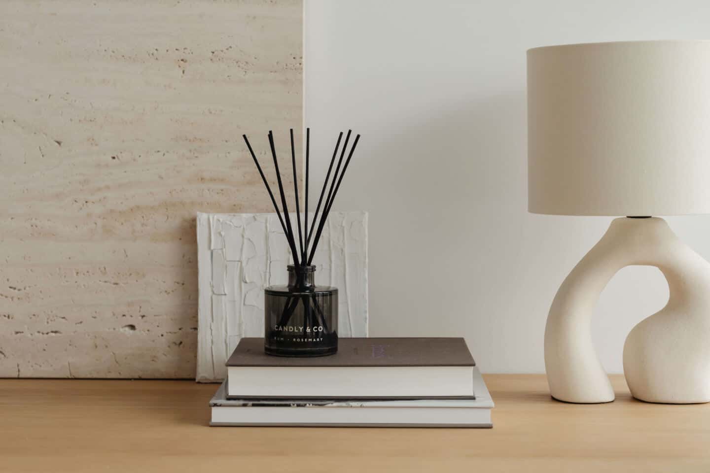 A reed diffuser on top of a pile of books with an abstract white lamp beside