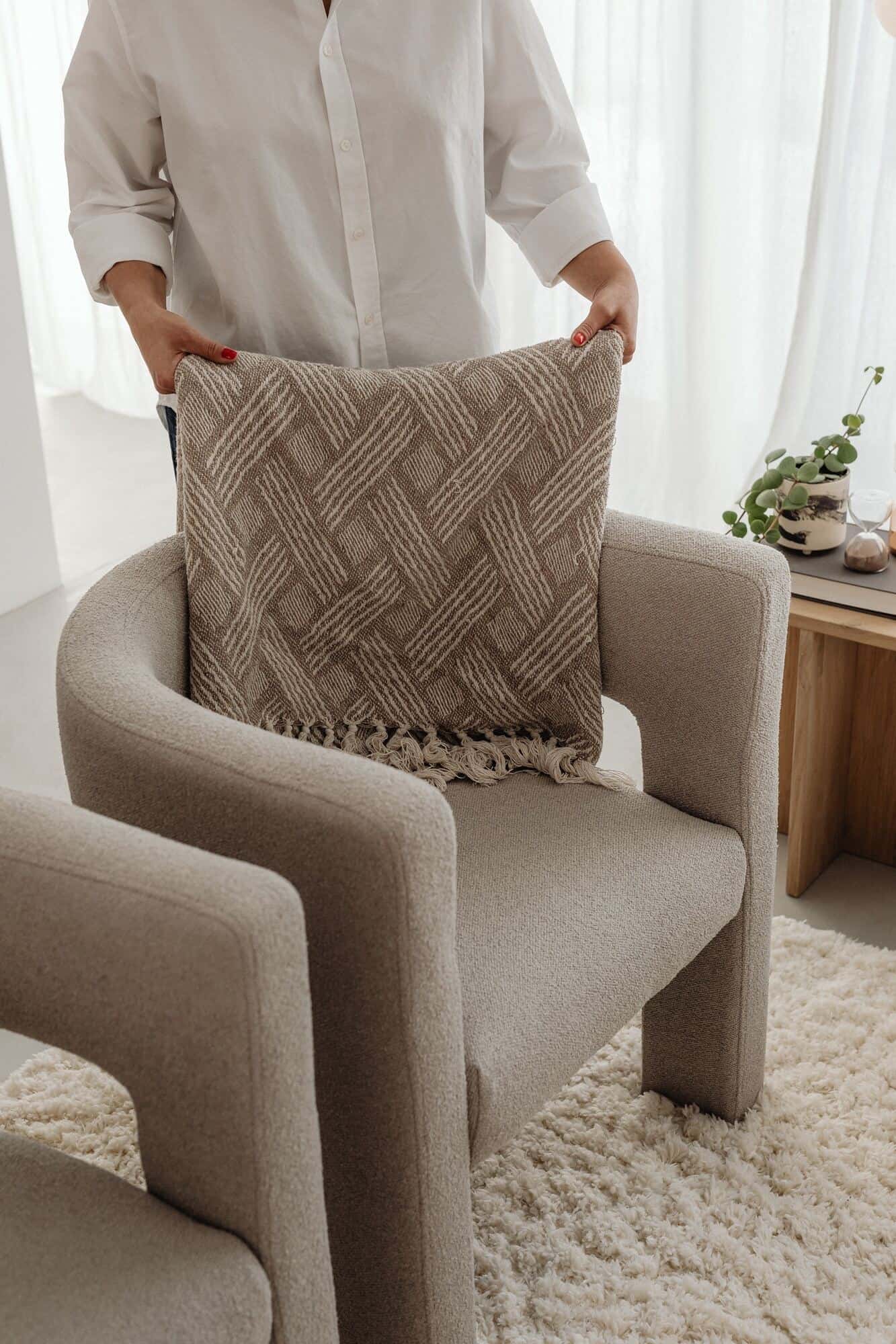 A woman lays a blanket on the back of a boucle armchair in a calming living space