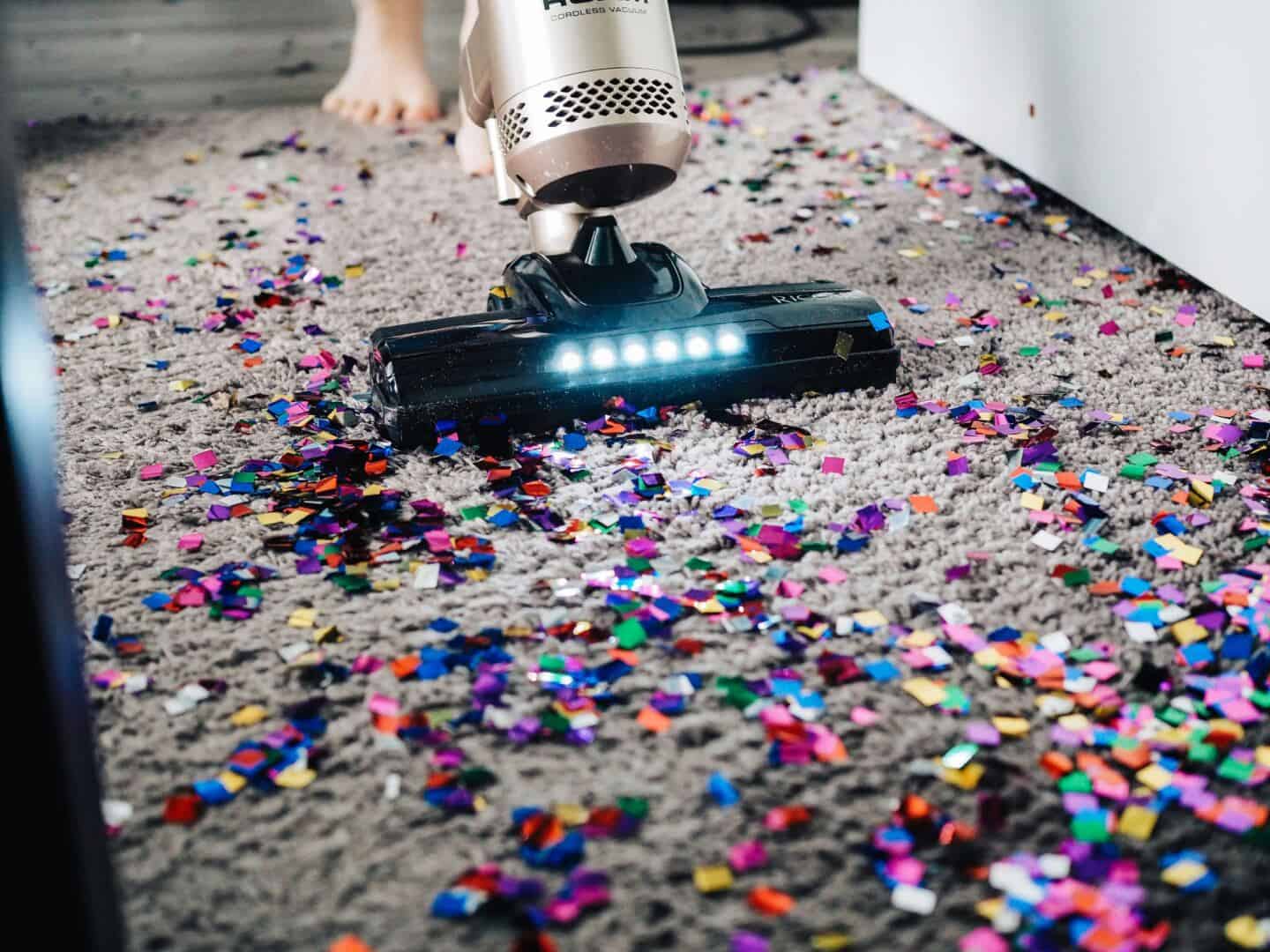 A barefoot person using a vacuum cleaner to hoover a carpet covered in confetti