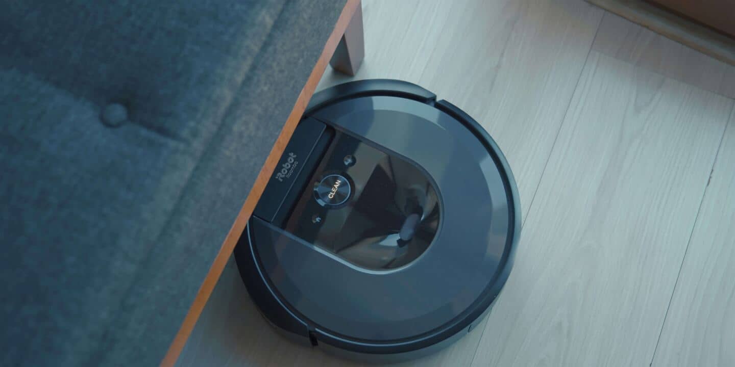 A robot vacuum cleaner half under a piece of furniture on a wooden floor