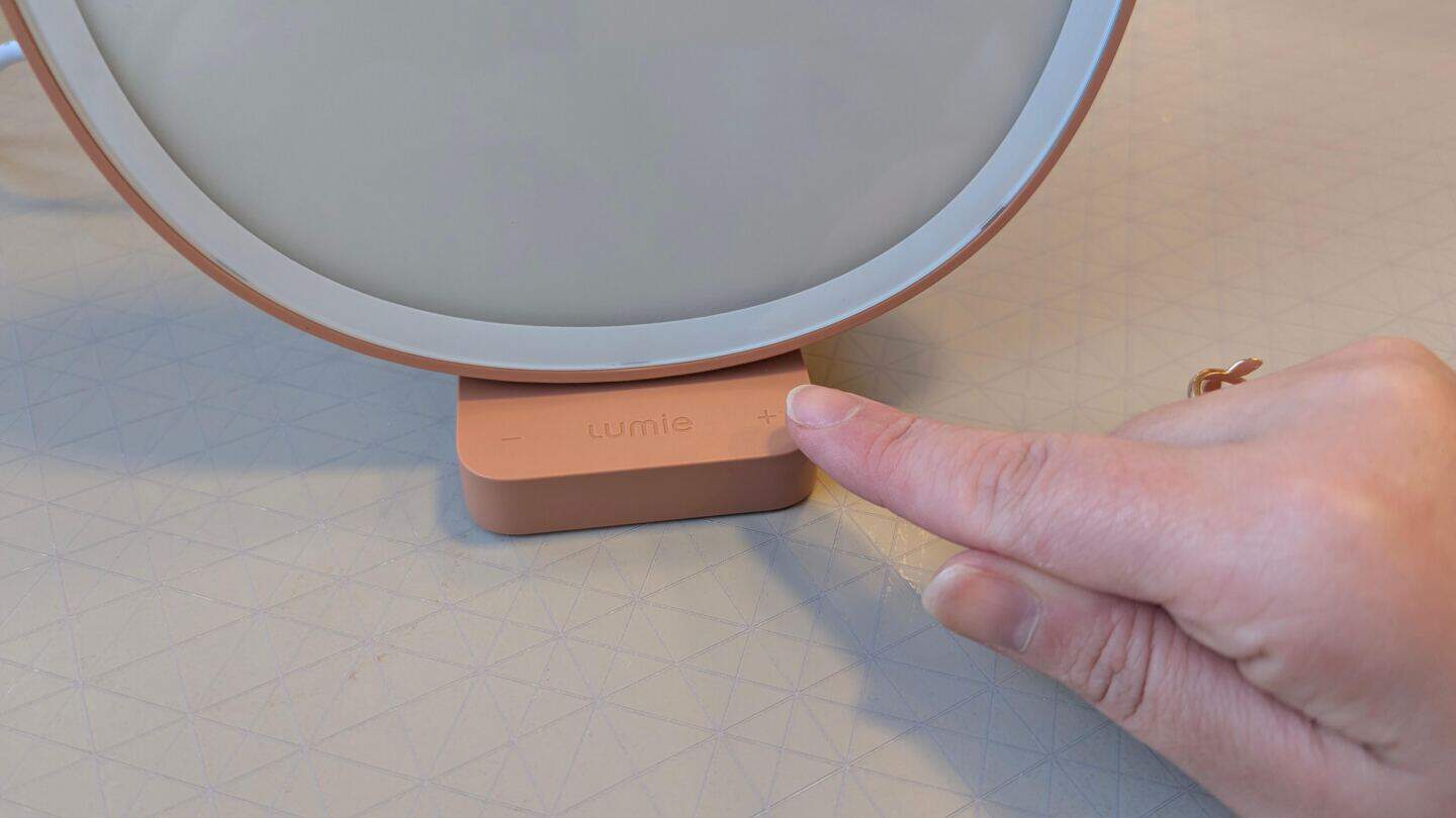 A close up photo of a woman's hand operating the Lumie Dash SAD Light