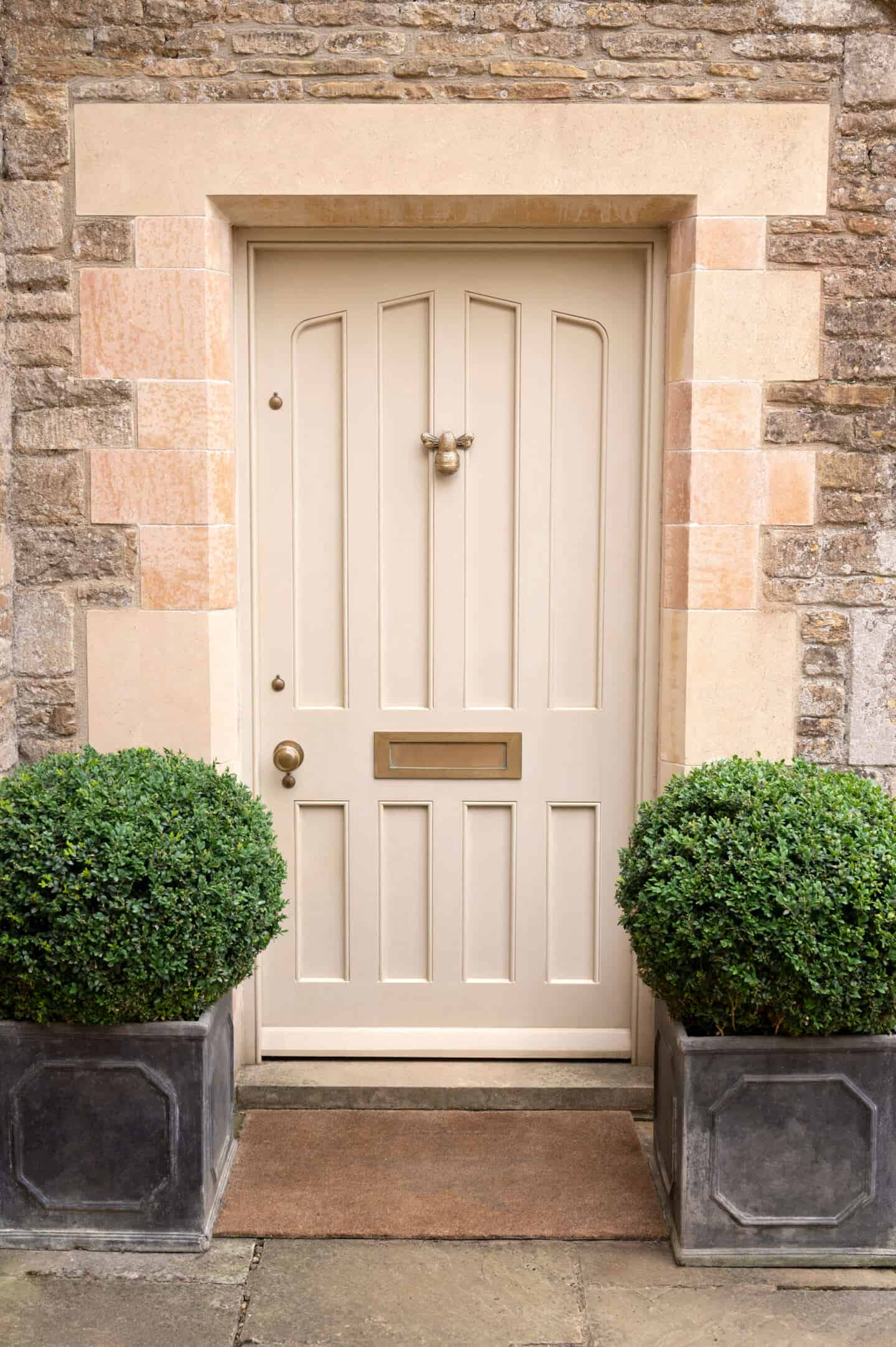 a beige front door with a brass bumble bee door knocker