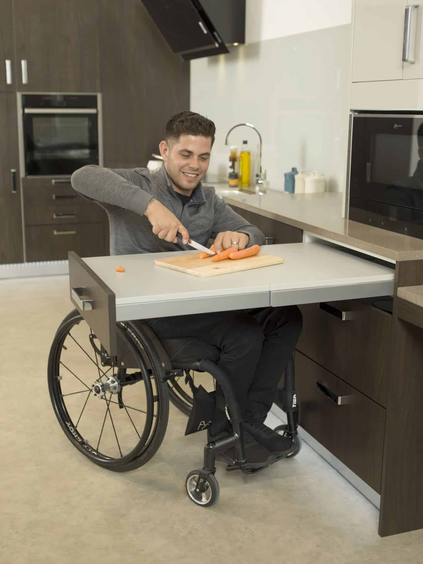 A man in a wheelchair choppig vegetables on a pullout worksurface in a Freedom kitchen by Symphony