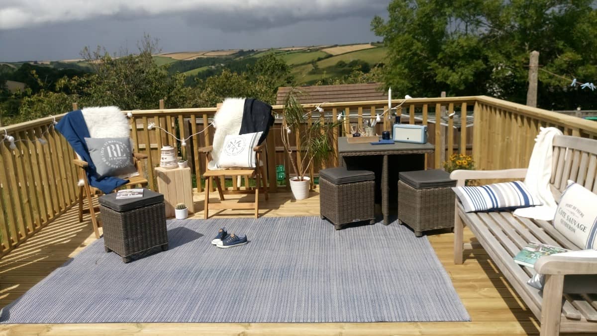 A nautical themed garden deck featuring composite dining cube, a wooden bench and two wooden chairs and a blue outdoor rug.