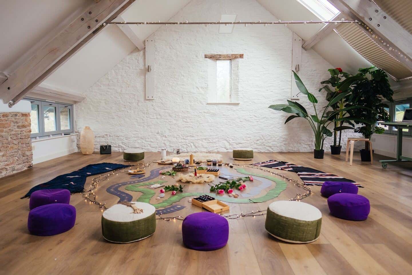 A studio with vaulted ceiling set up for a woman's circle with cushions on the floor, tarot cards, crystals, flowers and faux plants from Blooming Artificial