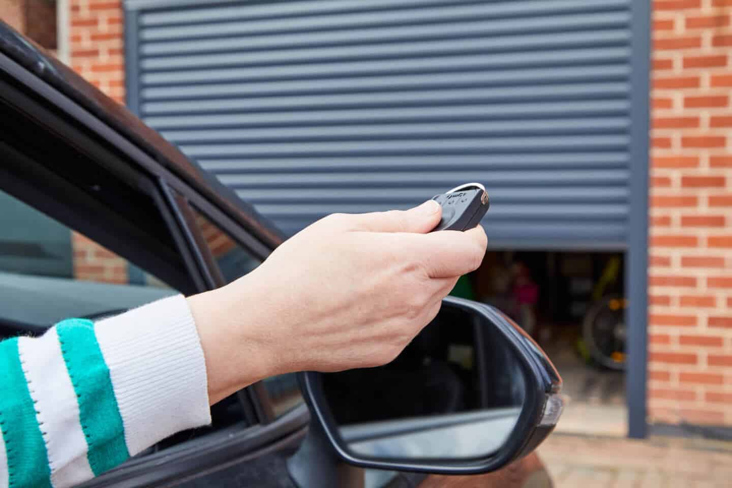 A man in a car operating an electric garage door with a remote control