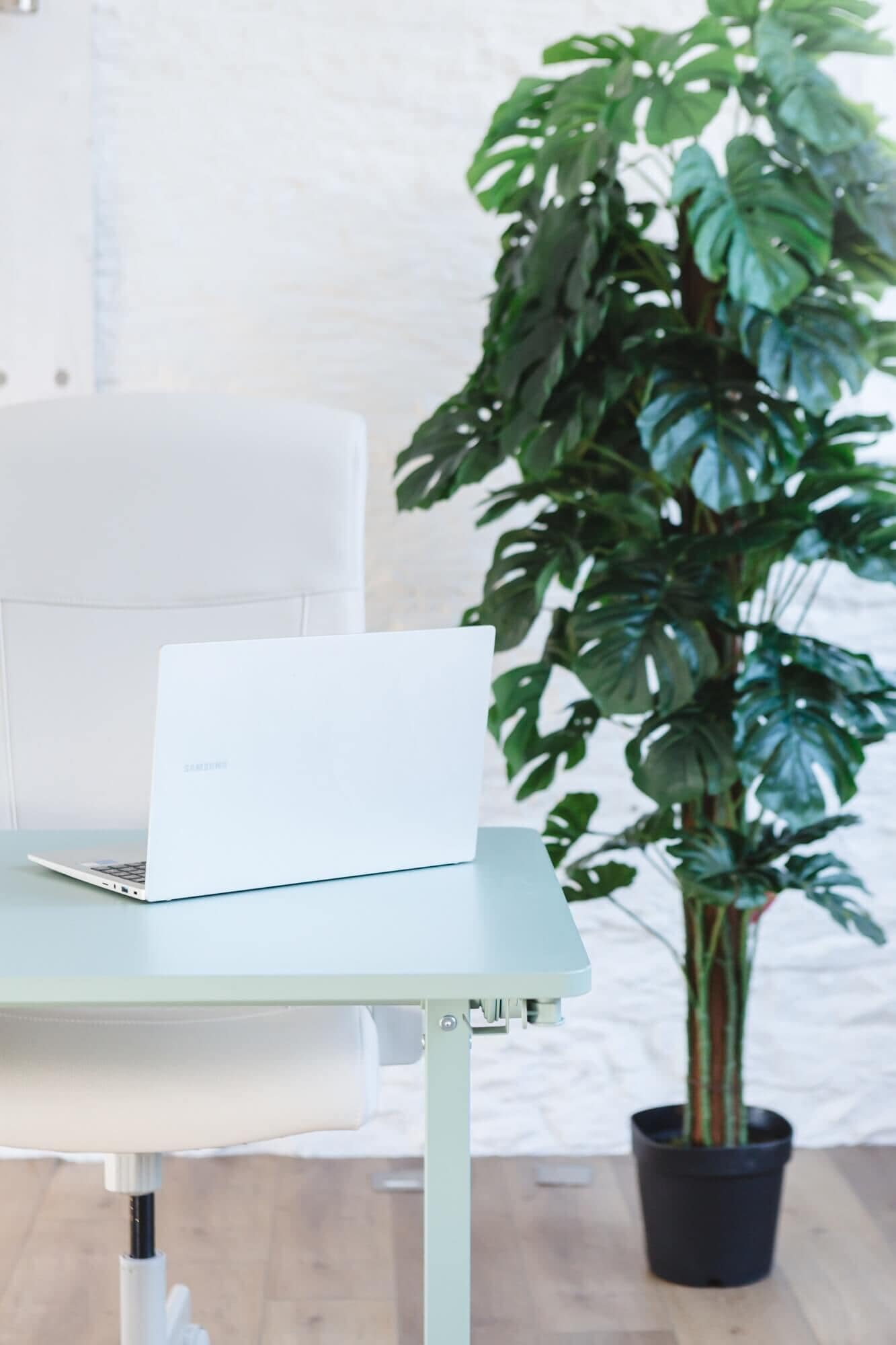 A desk and chair next to an artificial plant from Blooming Artificial in an office
