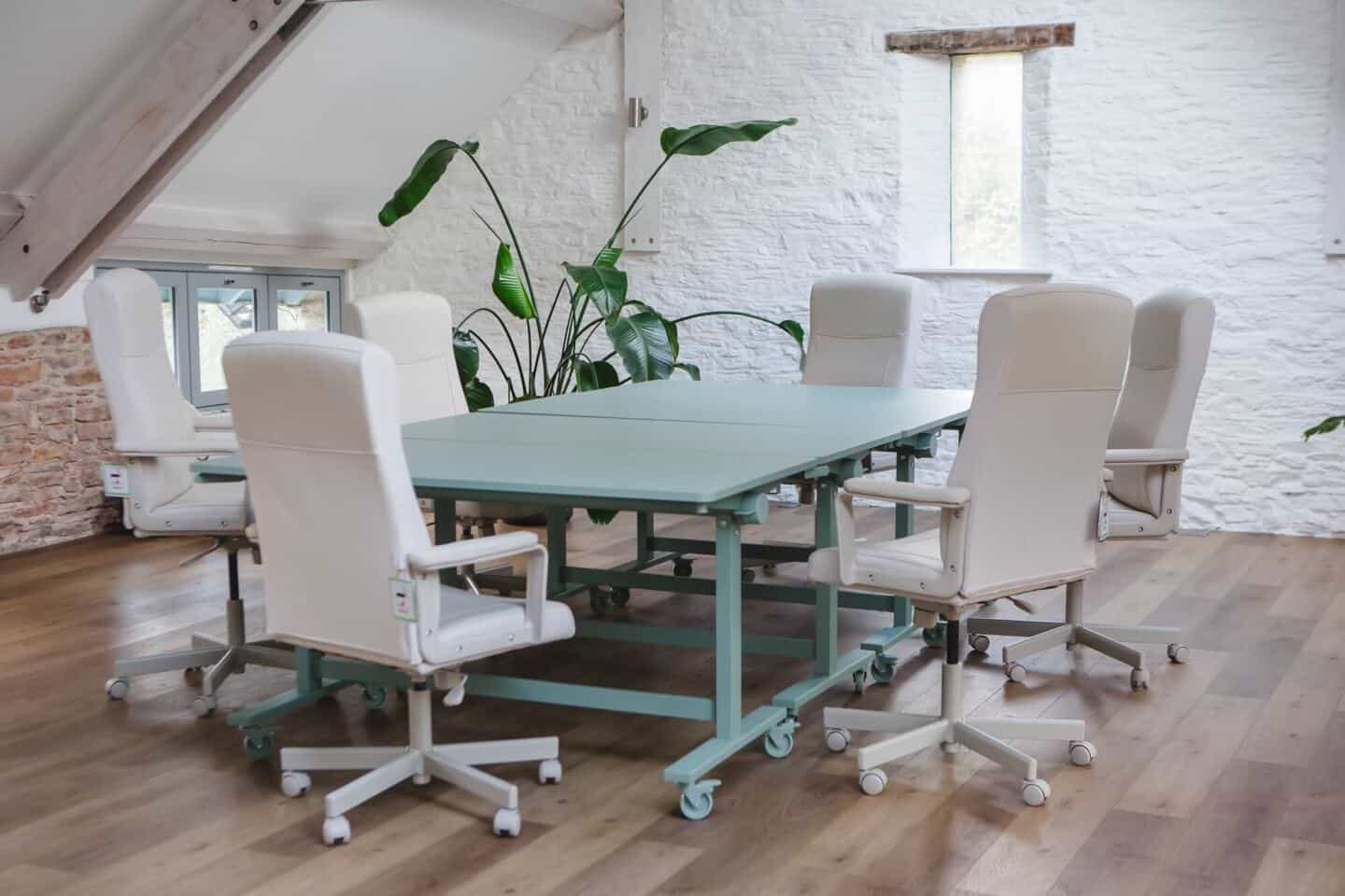 A large desk surrounded by chairs in an office with an artificial plant from Blooming Artificial in the background