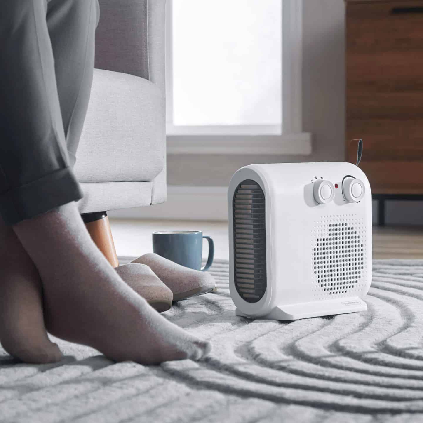 Fan heater on the floor next to a chair warming someone's feet