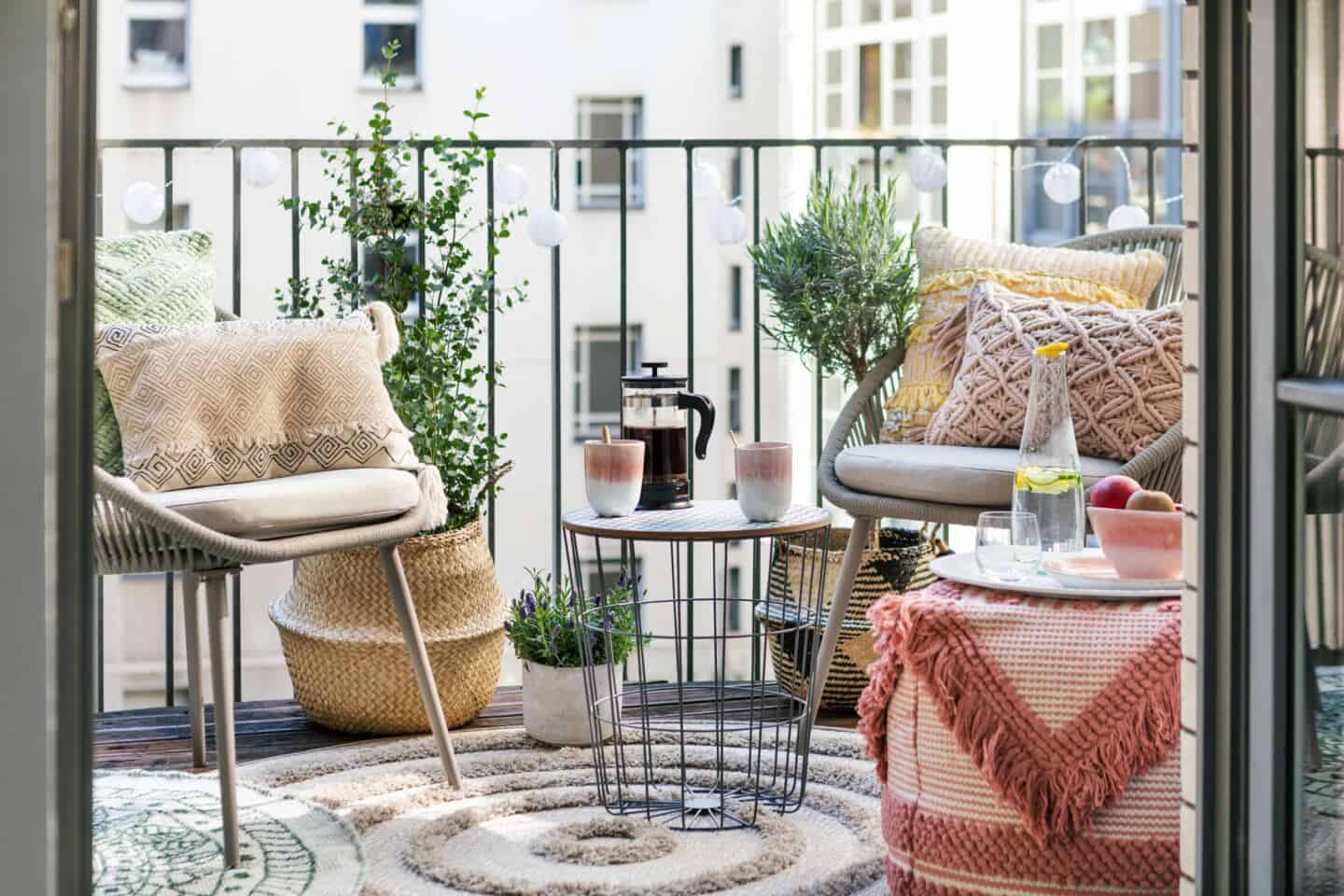 A bistro table and chairs and lots of textured cushions and rugs on a small balcony